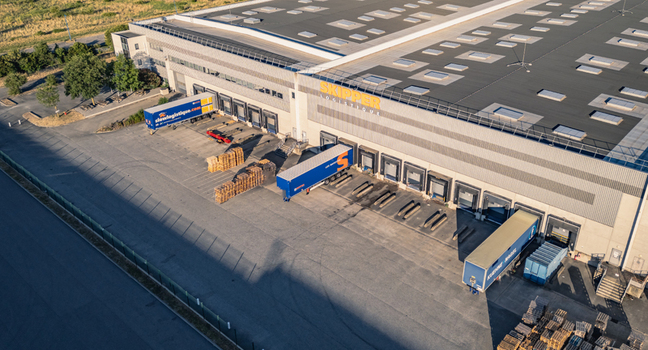 Le Pouzin France 04 July 2026 Aerial view of the SKIPPER Logistique warehouse and distribution center with loading docks parked semi trucks and wooden pallets in the yard. Le Pouzin France 04 July 2026 Aerial view of the SKIPPER Logistique warehouse and distribution center with loading docks parked semi trucks and wooden pallets in the yard.