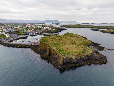 Aerial view of the coastal town of Stykkisholmur featuring a prominent grassy cliff with a lighthouse a small harbor with boats and surrounding volcanic landscape in Iceland. Aerial view of the coastal town of Stykkisholmur featuring a prominent grassy cliff with a lighthouse a small harbor with boats and surrounding volcanic landscape in Iceland.
