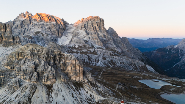 Aerial view of Tre Cime di Lavaredo peaks glowing in golden sunset light with alpine lakes and rocky terrain Auronzo di Cadore Veneto Italy. Aerial view of Tre Cime di Lavaredo peaks glowing in golden sunset light with alpine lakes and rocky terrain Auronzo di Cadore Veneto Italy.