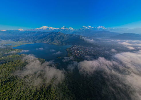 Aerial view of Phewa Lake and the city of Pokhara nestled beneath the snow capped peaks of the Annapurna mountain range under a clear blue sky Nepal.