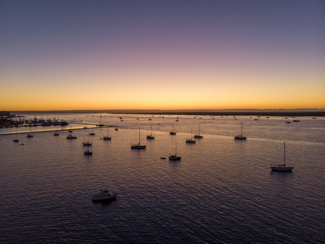 Aerial view of sailboats and yachts anchored in the calm bay at sunset near the Malecon de La Paz with a vibrant sky reflecting on the water in La Paz Baja California Sur Mexico.