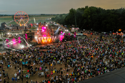 Herzogenaurach Germany 26 July 2025 Aerial view of the Open Beatz Festival featuring a large crowd a glowing Ferris wheel and a vibrant main stage with pyrotechnics at dusk.