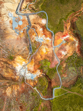 Aerial view of the colorful geothermal landscape with steaming vents mineral deposits and wooden boardwalks winding through the terrain in Iceland. Aerial view of the colorful geothermal landscape with steaming vents mineral deposits and wooden boardwalks winding through the terrain in Iceland.