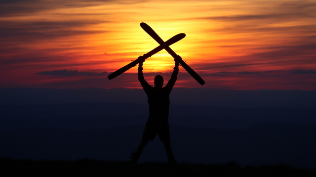 View of the silhouette of a person holding crossed skis above their head against a vibrant sunset at Colomby de Gex in Echenevex Auvergne Rhone Alpes France. View of the silhouette of a person holding crossed skis above their head against a vibrant sunset at Colomby de Gex in Echenevex Auvergne Rhone Alpes France.
