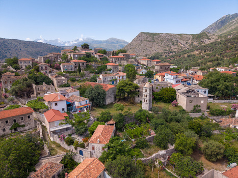 Aerial view of the historic hillside village featuring stone houses with red tiled roofs and a church tower nestled among green trees in Qeparo Fshat Vlore County Albania. Aerial view of the historic hillside village featuring stone houses with red tiled roofs and a church tower nestled among green trees in Qeparo Fshat Vlore County Albania.