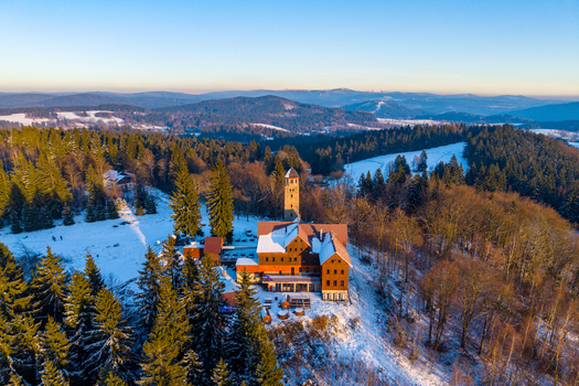 Aerial view of Bramberk lookout tower and mountain hotel surrounded by snow covered pine forests during golden hour in Lucany nad Nisou Liberec Region Czechia. Aerial view of Bramberk lookout tower and mountain hotel surrounded by snow covered pine forests during golden hour in Lucany nad Nisou Liberec Region Czechia.