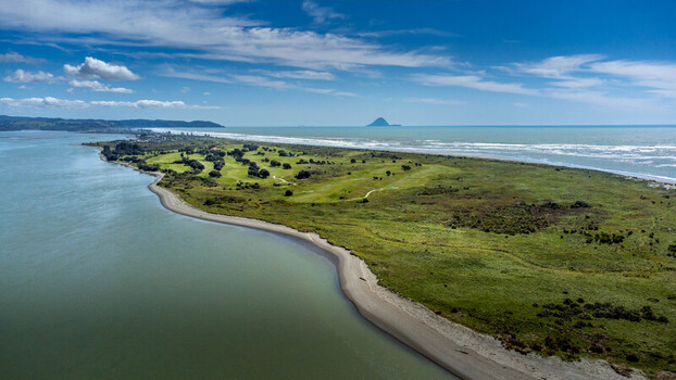 Aerial view of the coastal golf course at Ohope Beach featuring lush green fairways sand dunes and the Pacific Ocean under a blue sky in Ohope Bay of Plenty Region New Zealand.