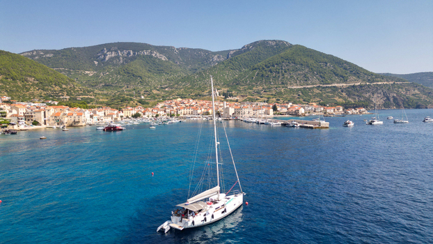 Aerial view of the harbor and coastal town of Komiza with a large white sailboat on the turquoise sea and green hills in the background Komiza Split Dalmatia County Croatia.