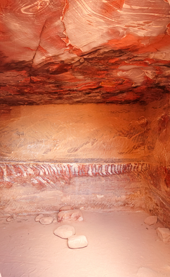 View of the interior of a historic rock cut chamber featuring intricate red and orange sandstone layers and natural rock formations in Wadi Musa Ma an Governorate Jordan. View of the interior of a historic rock cut chamber featuring intricate red and orange sandstone layers and natural rock formations in Wadi Musa Ma an Governorate Jordan.