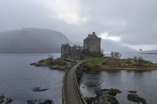 Aerial view of Eilean Donan Castle on its tidal island with the stone bridge and misty highland hills in Dornie Scotland United Kingdom.