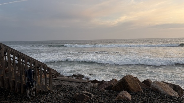 View of crashing waves on a rocky shoreline with wooden stairs under a soft sunset sky in Oceanside California United States. View of crashing waves on a rocky shoreline with wooden stairs under a soft sunset sky in Oceanside California United States.