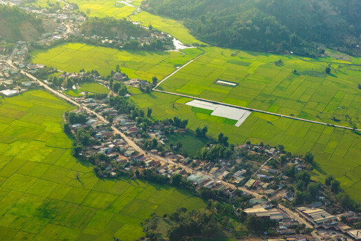 Aerial view of Lak Lake surrounded by lush green rice paddies and a small village with houses along a road in Lien Son Lak Dak Lak Vietnam. Aerial view of Lak Lake surrounded by lush green rice paddies and a small village with houses along a road in Lien Son Lak Dak Lak Vietnam.