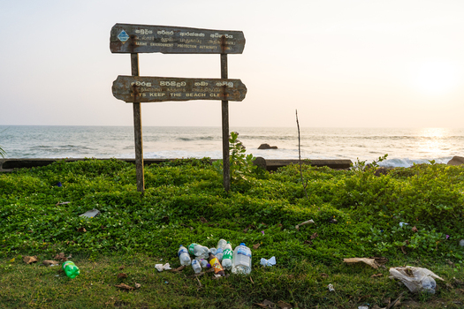 View of a wooden environmental protection sign standing over plastic litter on a grassy shore by the ocean in Galle Southern Province Sri Lanka.