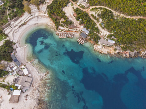 Aerial view of the turquoise waters of Ksamil bay with sandy beaches wooden structures and lush green hills in Ksamil Vlore County Albania. Aerial view of the turquoise waters of Ksamil bay with sandy beaches wooden structures and lush green hills in Ksamil Vlore County Albania.