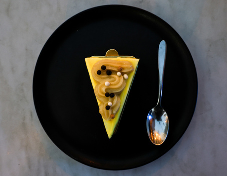 View of a slice of yellow cake topped with piped cream and chocolate pearls served on a black plate with a silver spoon in San Jose del Cabo Baja California Sur Mexico.