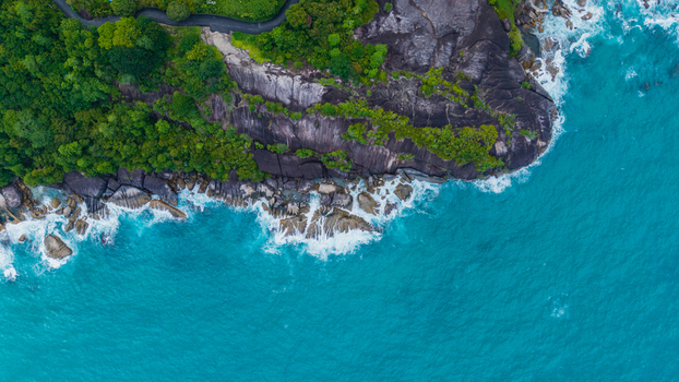 Aerial view of Anse Soleil Beachcomber Hotel nestled on a rocky cliffside with lush tropical vegetation overlooking the turquoise waters of the Indian Ocean Mahe Baie Lazare Seychelles.