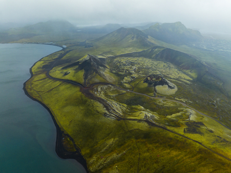 Aerial view of a dramatic landscape where the inky blue waters meet the vibrant green hills under a misty sky Highlands Iceland.