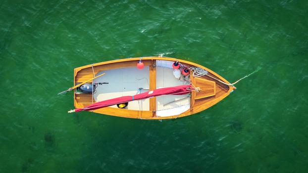 Aerial view of a wooden boat with a red sail contrasts against the emerald water creating a vivid scene of maritime beauty Carantec Brittany France.