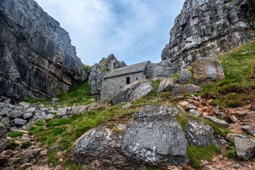 View of Saint Govan s Chapel built into the rugged limestone cliffs with green grass and a cloudy sky St. Govan s Head Wales United Kingdom. View of Saint Govan s Chapel built into the rugged limestone cliffs with green grass and a cloudy sky St. Govan s Head Wales United Kingdom.