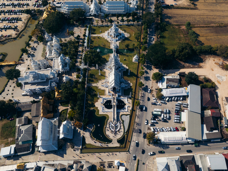 Aerial view of the intricate white architecture of Wat Rong Khun temple complex surrounded by green lawns and trees in Pa O Don Chai Chiang Rai Thailand. Aerial view of the intricate white architecture of Wat Rong Khun temple complex surrounded by green lawns and trees in Pa O Don Chai Chiang Rai Thailand.
