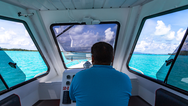 View of a boat captain steering through the turquoise waters of a tropical lagoon in Bora Bora Leeward Islands French Polynesia.