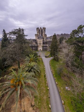 Aerial view of Butron Castle surrounded by lush trees palm trees and a winding path under a cloudy sky in Butroi Euskadi Spain. Aerial view of Butron Castle surrounded by lush trees palm trees and a winding path under a cloudy sky in Butroi Euskadi Spain.