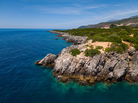 Aerial view of the rocky coastline of Aquarium Beach with turquoise waters and lush green vegetation under a clear blue sky in Jala Vlore County Albania.