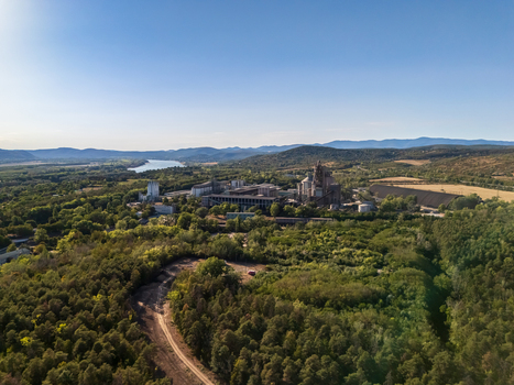 Aerial view of a cement manufacturing plant with silos and processing towers amid summer woodland near the Danube River Vac Hungary with hills in the distance. Aerial view of a cement manufacturing plant with silos and processing towers amid summer woodland near the Danube River Vac Hungary with hills in the distance.