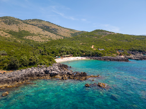 Aerial view of Aquarium Beach with turquoise water rocky shores and lush green hills in Jala Vlore County Albania.