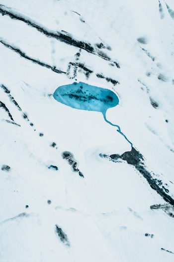 Aerial view of Vatnajokull glacier featuring a vibrant blue meltwater pool surrounded by intricate ice cracks and textures in Iceland.