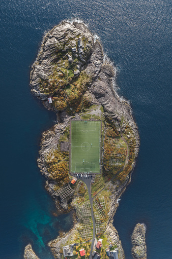 Aerial view of the iconic Henningsvaer football field situated on a rocky island surrounded by the deep blue waters of the Norwegian Sea in Henningsvaer Nordland Norway. Aerial view of the iconic Henningsvaer football field situated on a rocky island surrounded by the deep blue waters of the Norwegian Sea in Henningsvaer Nordland Norway.