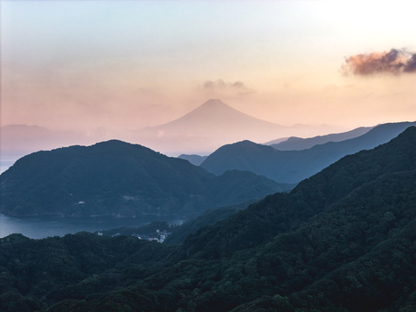 Aerial view of Mount Fuji rising above the misty mountain ridges and the coastline of Suruga Bay during a soft sunset in Nishiizu Dogashima Coast Shizuoka Japan.