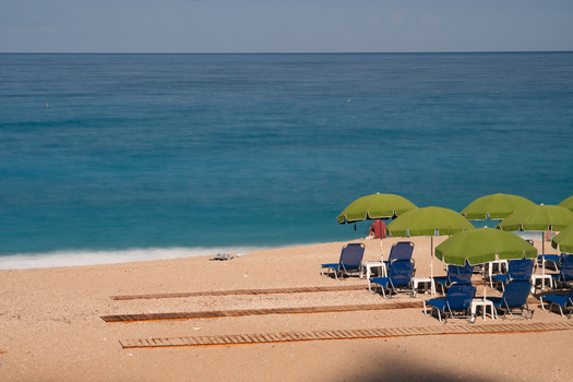 View of turquoise waters meet the sandy shore under a cerulean sky with umbrellas casting shadows on the beach Kathisma beach Lefkada Greece. View of turquoise waters meet the sandy shore under a cerulean sky with umbrellas casting shadows on the beach Kathisma beach Lefkada Greece.