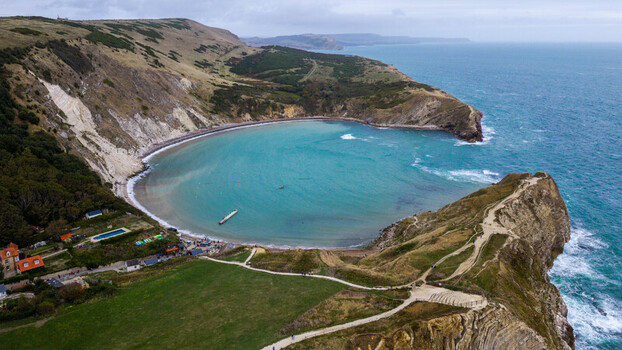 Aerial view of Lulworth Cove featuring a distinctive horseshoe shaped bay with turquoise water dramatic limestone cliffs and grassy headlands along the coast of the United Kingdom.