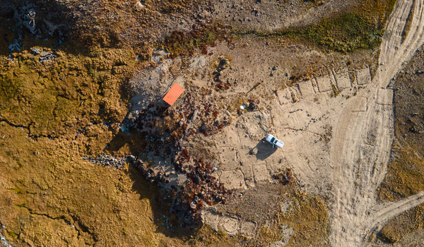 Aerial view of Deosai Plains featuring a small structure with an orange roof a parked white vehicle and rugged terrain with dirt tracks in Skardu Gilgit Pakistan. Aerial view of Deosai Plains featuring a small structure with an orange roof a parked white vehicle and rugged terrain with dirt tracks in Skardu Gilgit Pakistan.