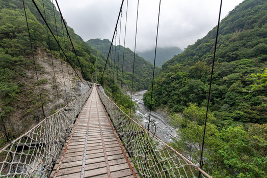 View of the suspension bridge spanning the river canyon in Taroko National Park surrounded by lush green mountains and steep cliffs in Xiulin Township Hualien County Taiwan.