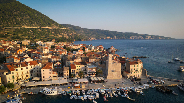 Aerial view of the historic harbor and stone houses with the Kastel tower and boats moored in the blue water Komiza Split Dalmatia County Croatia.