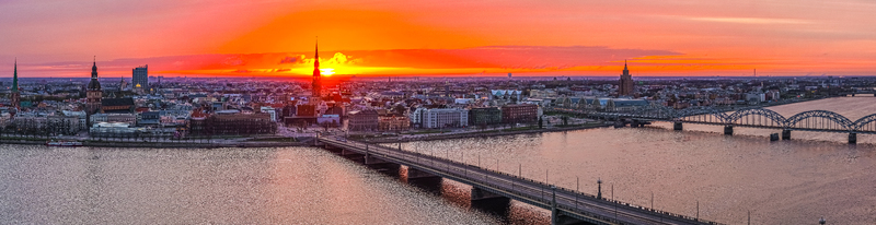 Aerial view of the Riga skyline at sunset featuring the Daugava River the Stone Bridge and historic church spires under a vibrant orange sky in Riga Latvia. Aerial view of the Riga skyline at sunset featuring the Daugava River the Stone Bridge and historic church spires under a vibrant orange sky in Riga Latvia.