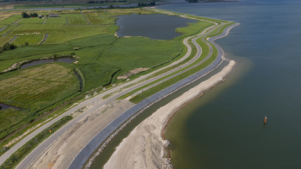 Aerial view of the coastal dike and winding road along the Markermeer with green polder fields and sandy shoreline in Uitdam North Holland Netherlands.