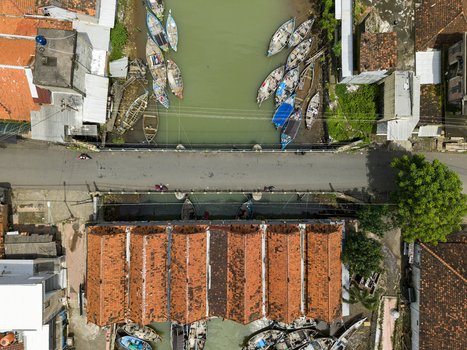 Aerial view of boats resting in the river near the market and bridge contrasting with the vibrant orange roofs of the buildings Jepara Central Java Indonesia.