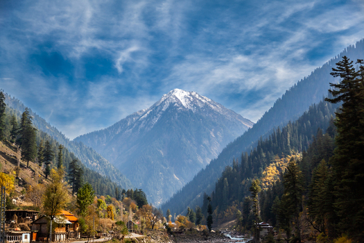 View of the snow capped mountain peak of Neelum Valley surrounded by dense pine forests and a small village under a blue sky in Arang Kel Azad Kashmir Pakistan. View of the snow capped mountain peak of Neelum Valley surrounded by dense pine forests and a small village under a blue sky in Arang Kel Azad Kashmir Pakistan.