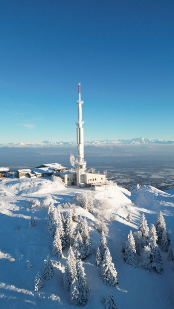 Aerial view of the telecommunications tower at Col de la Faucille surrounded by snow covered pine trees and mountain slopes in Gex Auvergne Rhone Alpes France. Aerial view of the telecommunications tower at Col de la Faucille surrounded by snow covered pine trees and mountain slopes in Gex Auvergne Rhone Alpes France.