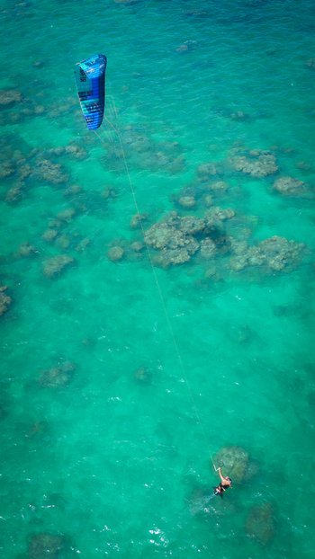 Aerial view of a kite surfer gliding over the clear turquoise waters dotted with visible reefs off Lanikai Beach Kailua Hawaii United States. Aerial view of a kite surfer gliding over the clear turquoise waters dotted with visible reefs off Lanikai Beach Kailua Hawaii United States.