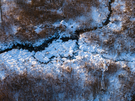 Aerial view of a small stream winding through snow covered reeds and dry winter vegetation under bright sunlight Lithuania. Aerial view of a small stream winding through snow covered reeds and dry winter vegetation under bright sunlight Lithuania.