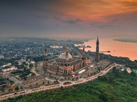 Aerial view of the Baitul Muttaqien Mosque at the East Kalimantan Islamic Center featuring its grand dome and minarets near the river at sunset in Samarinda East Kalimantan Indonesia.