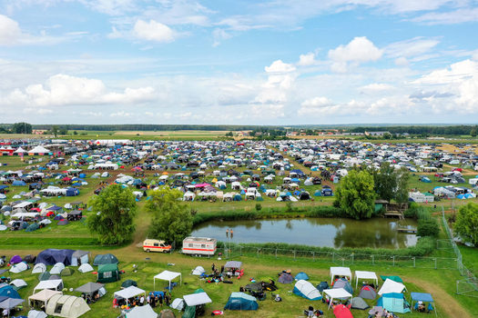 Aerial view of the Open Beatz Festival campsite featuring thousands of colorful tents a small pond and lush green trees under a bright cloudy sky in Herzogenaurach Bayern Germany. Aerial view of the Open Beatz Festival campsite featuring thousands of colorful tents a small pond and lush green trees under a bright cloudy sky in Herzogenaurach Bayern Germany.
