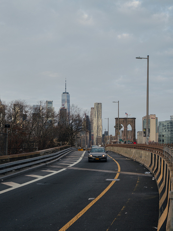 View of the Brooklyn Bridge with a car driving on the road and the New York City skyline in the background New York New York United States.