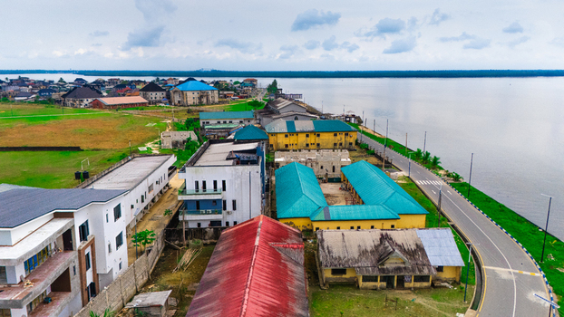 Aerial view of a coastal town in Rivers Nigeria featuring residential buildings with colorful roofs a paved road running along the water and lush green spaces.