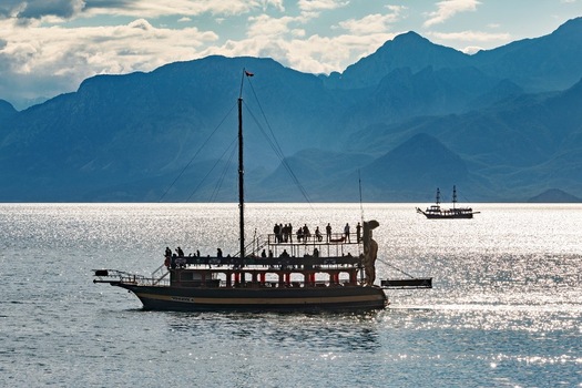 View of a tourist boat filled with people sailing on the sparkling Mediterranean Sea with the Taurus Mountains in the background in Antalya Antalya Turkey.