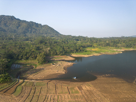 Aerial view of the Karanganyar reservoir area featuring terraced agricultural fields lush green hills and calm water in Wadaslintang Central Java Indonesia. Aerial view of the Karanganyar reservoir area featuring terraced agricultural fields lush green hills and calm water in Wadaslintang Central Java Indonesia.